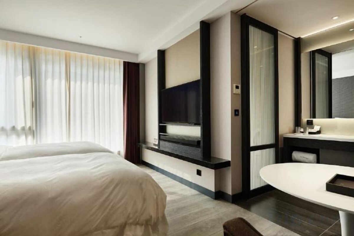 A modern hotel room with a large bed, a television, a bathroom with a mirror, and a small table.