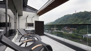 A balcony with two lounge chairs, a glass partition, and a view of a cityscape and hills. - The Tango Taipei Jiantan (Taipei)