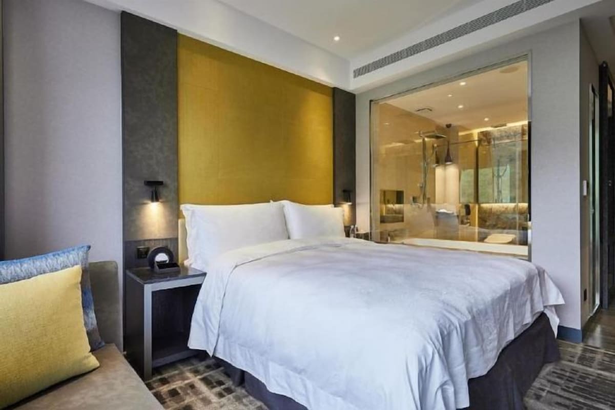 A modern hotel room with a large bed, a nightstand, and a glass shower area.