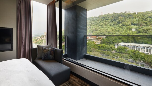 A modern hotel room with a large window offering a view of a lush green hillside and a distant building. - The Tango Taipei Jiantan (Taipei)