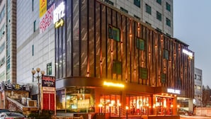 Um hotel moderno com um grande letreiro 'Grand Open', vários andares e uma entrada bem iluminada.