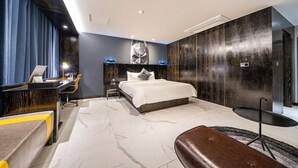 Quarto de hotel moderno com uma cama grande, uma escrivaninha, uma cadeira e uma pequena mesa.