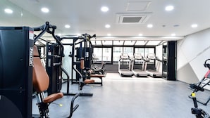 Uma academia com diversos equipamentos de ginástica, esteiras e um amplo janelão que oferece iluminação natural.