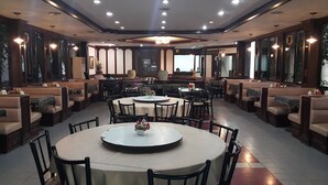 A spacious dining area with multiple round tables and booths, featuring a central chandelier and large windows. - Phuphaya Hotel (Pak Chong)