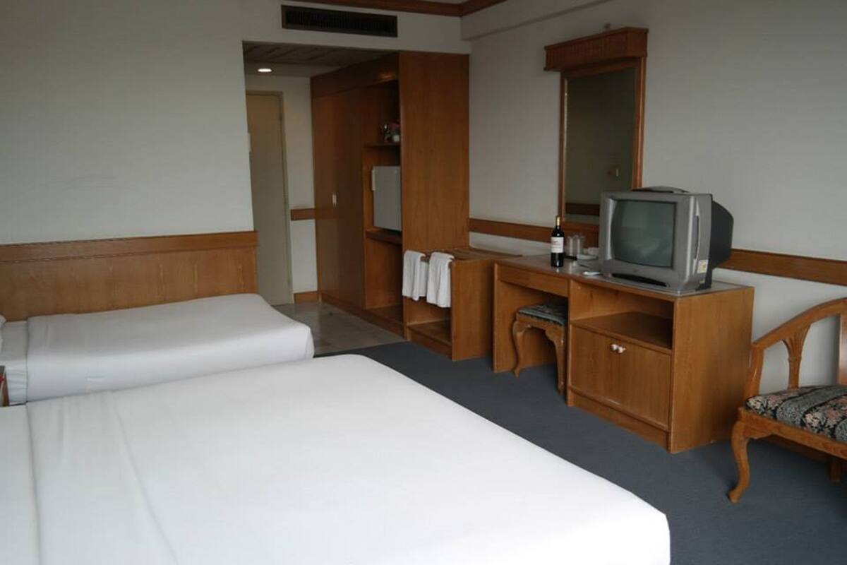 Una habitación de hotel con dos camas, un escritorio, un televisor, una silla y un espejo.