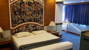 A hotel room with a large bed, two bedside tables with lamps, a floral-patterned headboard, and a view of the outside through a window with curtains. - Phuphaya Hotel (Pak Chong)