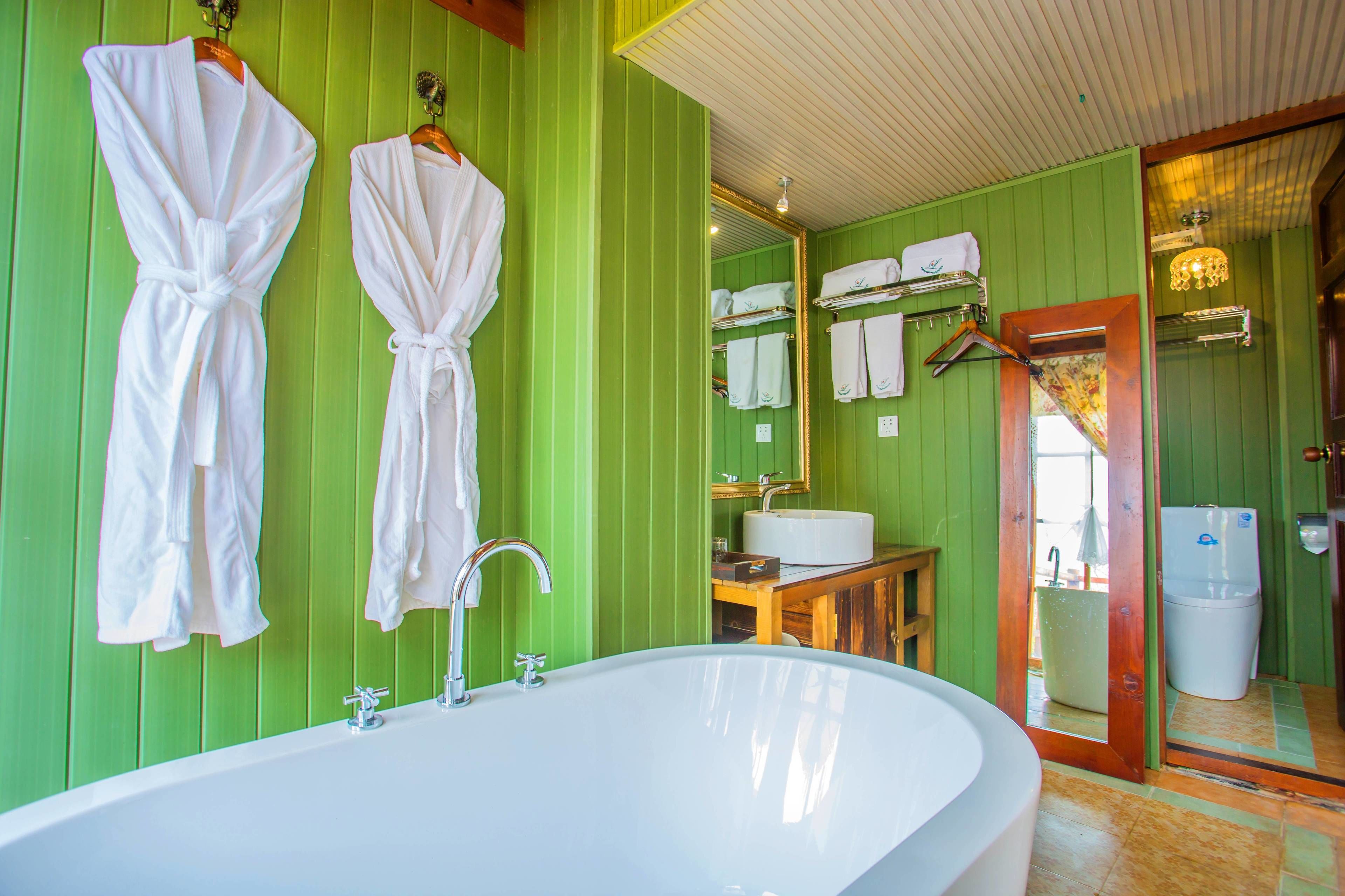 Un baño con una bañera grande, paredes verdes y toallas blancas colgadas en un perchero.