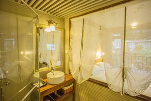 A bathroom with a glass shower enclosure, a round sink, and a mirror with a light fixture. - Lugu Lake Love Inn (Lijiang)