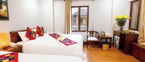 A hotel room with two beds, a desk, a chair, a small fridge, and a window with curtains.