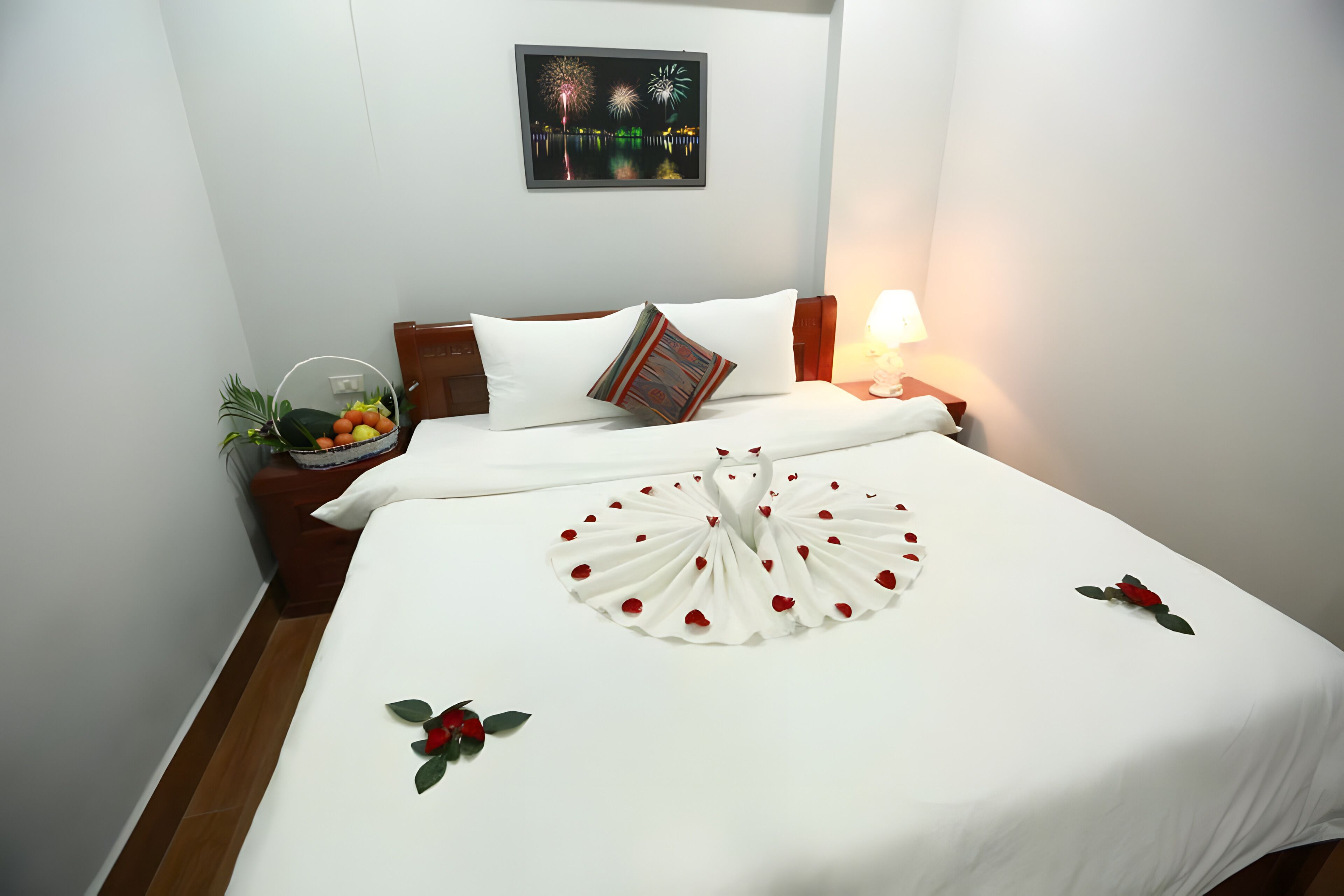 A hotel room with a neatly made bed, a nightstand with a lamp, a wall-mounted picture, and a small plant on the nightstand.