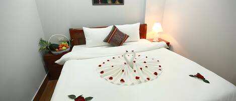 A hotel room with a neatly made bed, a nightstand with a lamp, a wall-mounted picture, and a small plant on the nightstand.