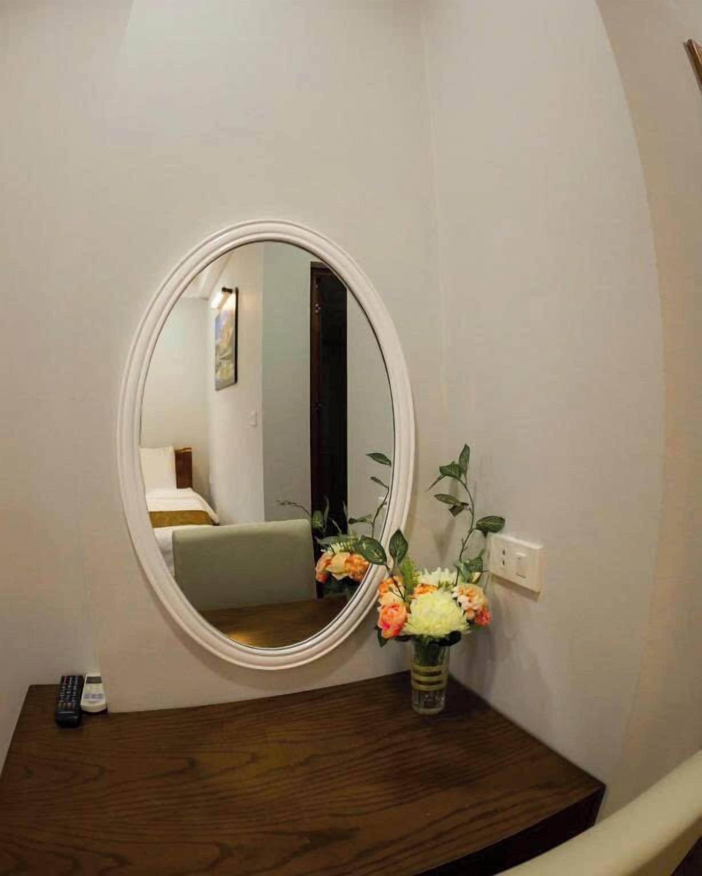 A bathroom with a round mirror, a wooden vanity, and a vase with flowers.