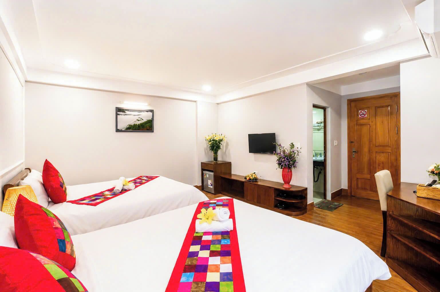A hotel room with two beds, a TV, a desk, and a door.