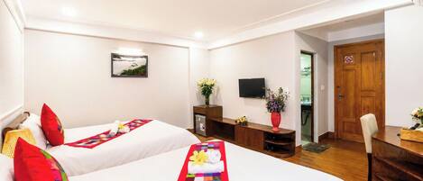 A hotel room with two beds, a TV, a desk, and a door.