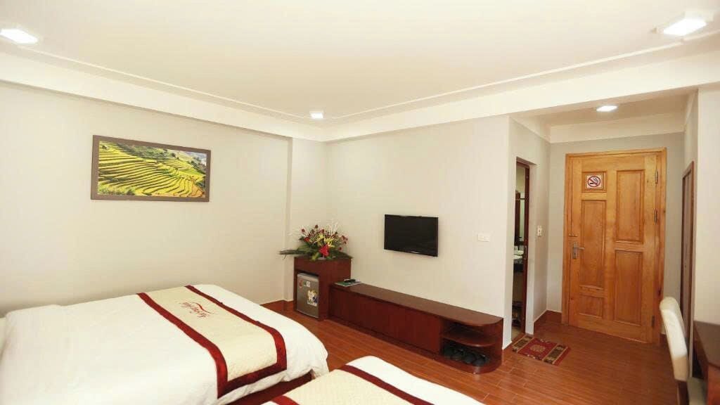 Habitación de hotel con dos camas, un televisor, un armario de madera y una puerta con letrero de no fumar.