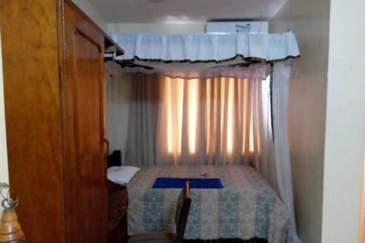 Un dormitorio con una cama, una silla, una puerta de madera y una cortina.