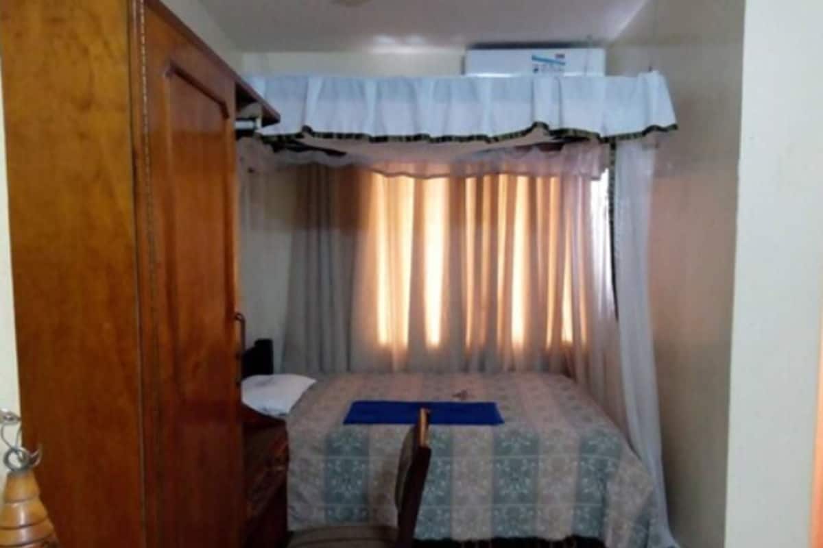 Un dormitorio con una cama, una silla, una puerta de madera y una cortina.