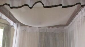 Ein Einzelbett mit Moskitonetz, einer blauen Matte und zwei Kissen.