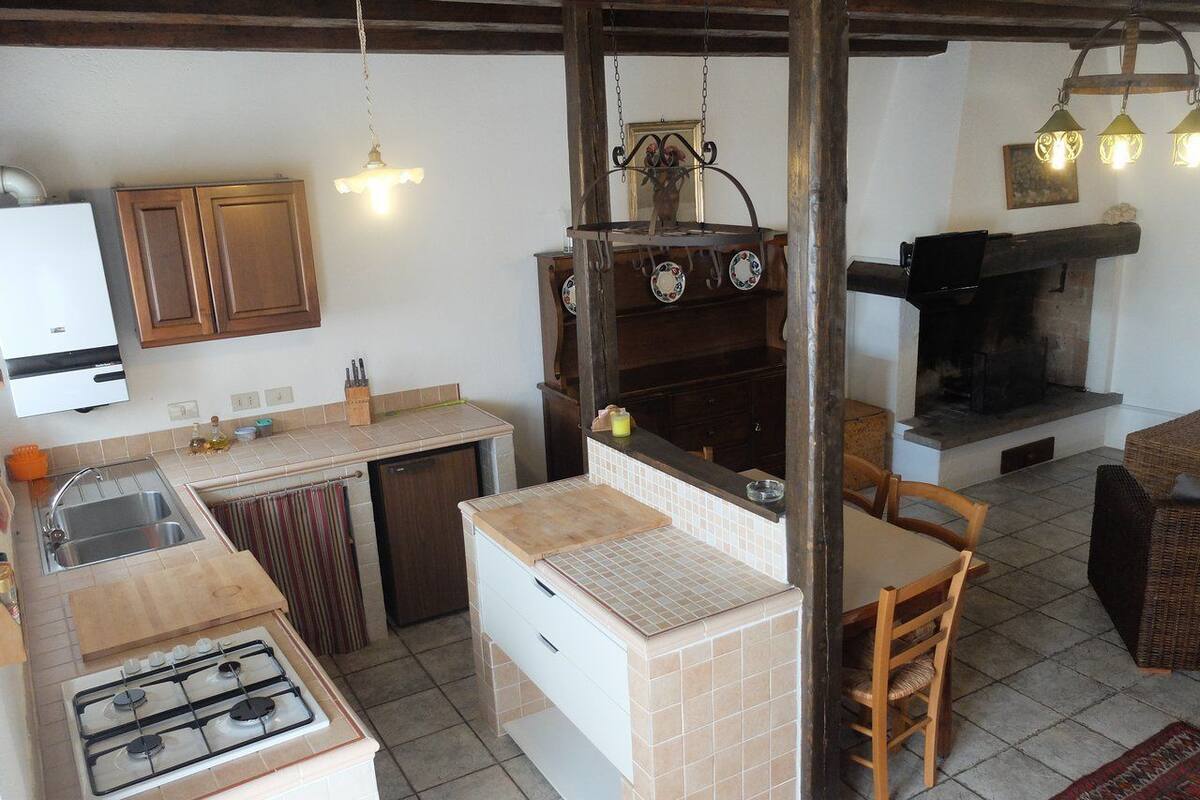 A compact kitchen with a gas stove, wooden cabinets, a dining table with chairs, and a hanging light fixture.