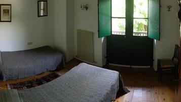 A room with two beds, a radiator, a window with green shutters, a chair, and a door.
