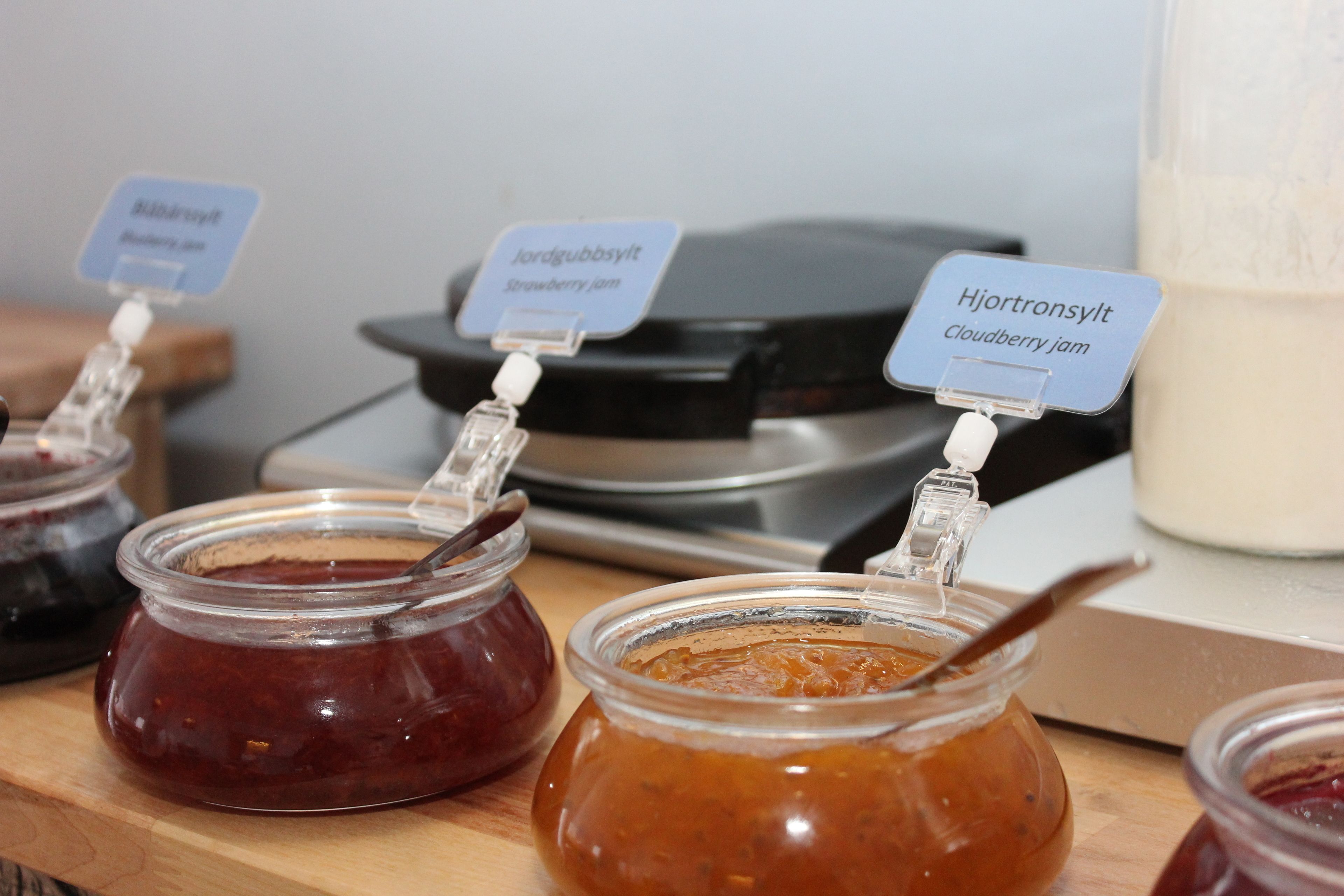 Tres botes de mermelada con etiquetas que indican los sabores: fresa, arándano rojo y frambuesa.