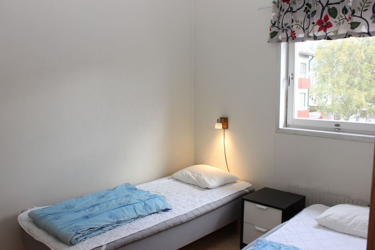 Habitació petita amb un llit individual, una finestra, una taula de nit i un radiador.
