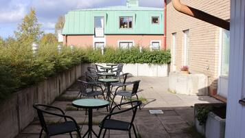 An outdoor patio with tables and chairs, a brick wall, and a building with a green roof in the background.