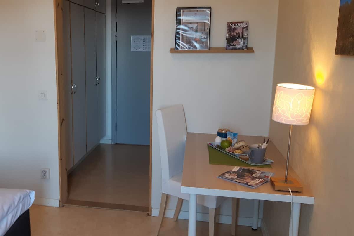 Habitació d'hotel amb un llit, una taula de treball amb una làmpada, una cadira i una taula petita amb aperitius.