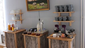 Een ontbijtbuffet met diverse etenswaren en toevoegingen, een schilderij van een berglandschap en planken met bekers en mokken.