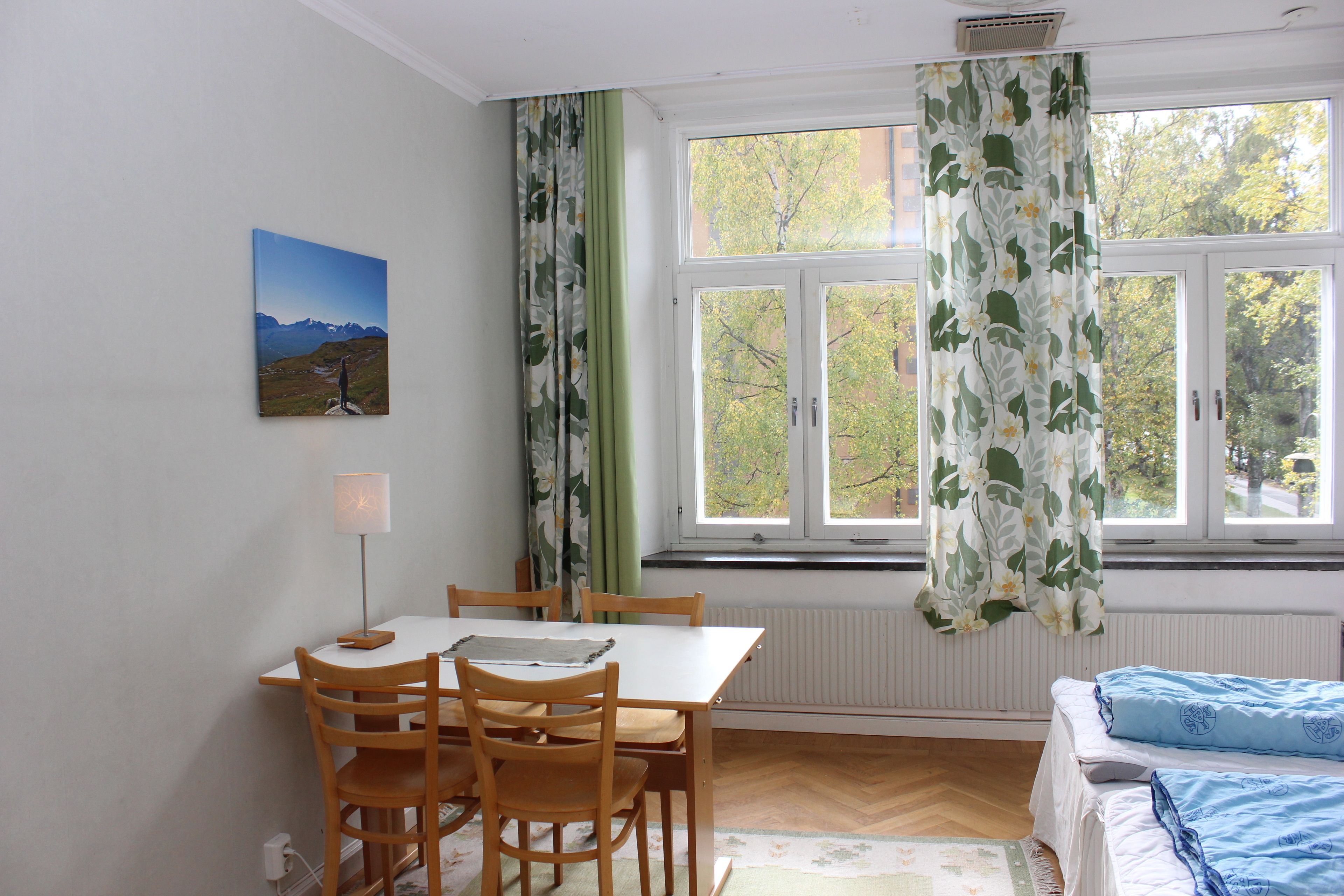 Una habitación con una mesa de comedor, sillas, una cama y un ventanal con cortinas.