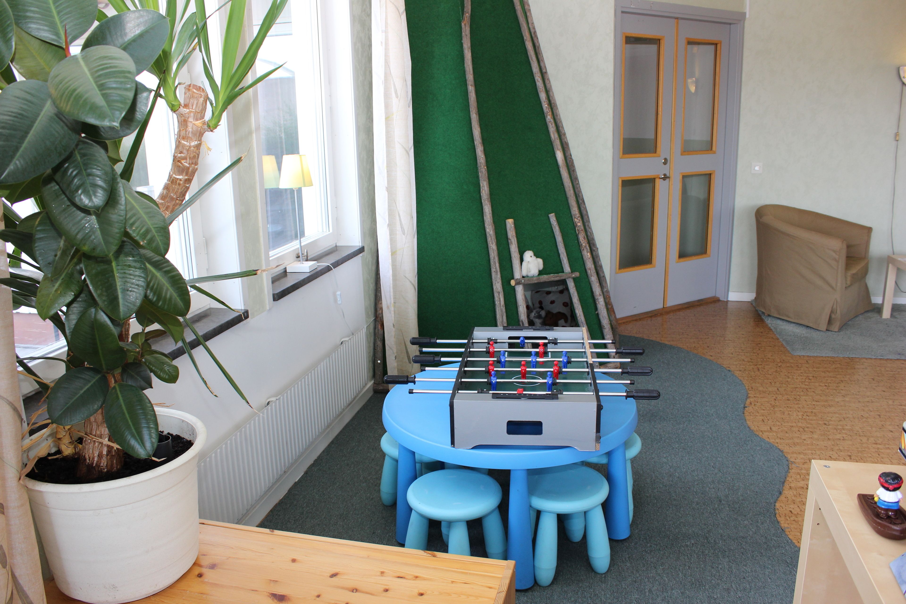 A room with a foosball table, a potted plant, and a window with curtains.