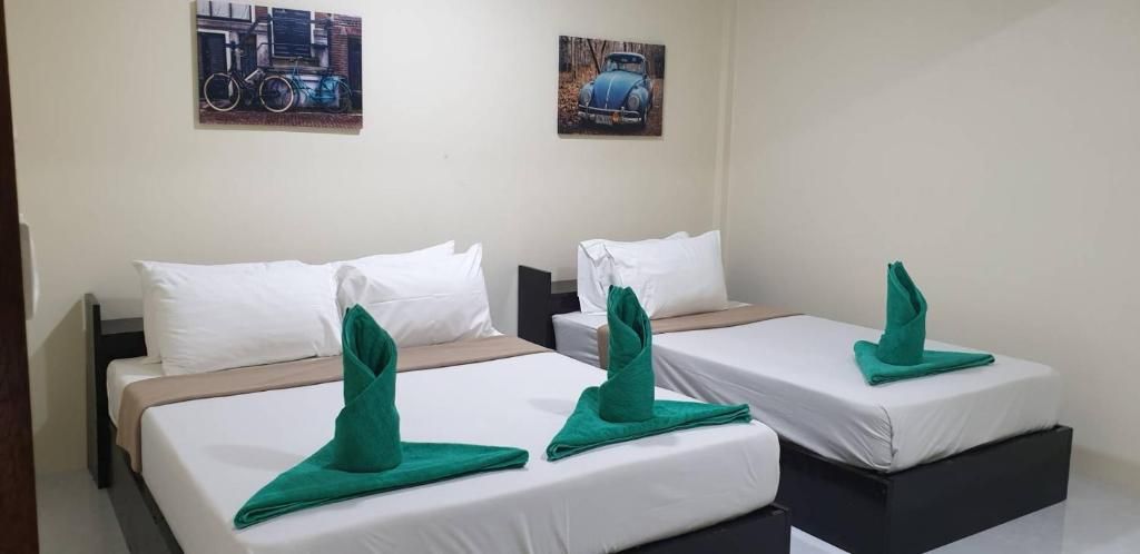 Habitación de hotel con dos camas, cada una con ropa blanca y toallas verdes dobladas. Hay dos cuadros en la pared, uno de una bicicleta y otro de un coche.