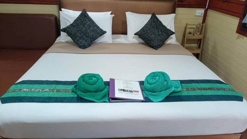 Una cama bien hecha con edredón blanco, dos almohadas, una colcha a rayas verdes y azules, y dos toallas enrolladas.