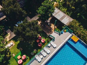 Eine Vogelperspektive zeigt ein Resort mit Swimmingpool, Liegestühlen und einem Garten.