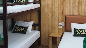 Een hotelkamer met stapelbedden en een eenpersoonsbed, beide met witte beddengoed en kussens met de tekst 'Wish' erop geborduurd.