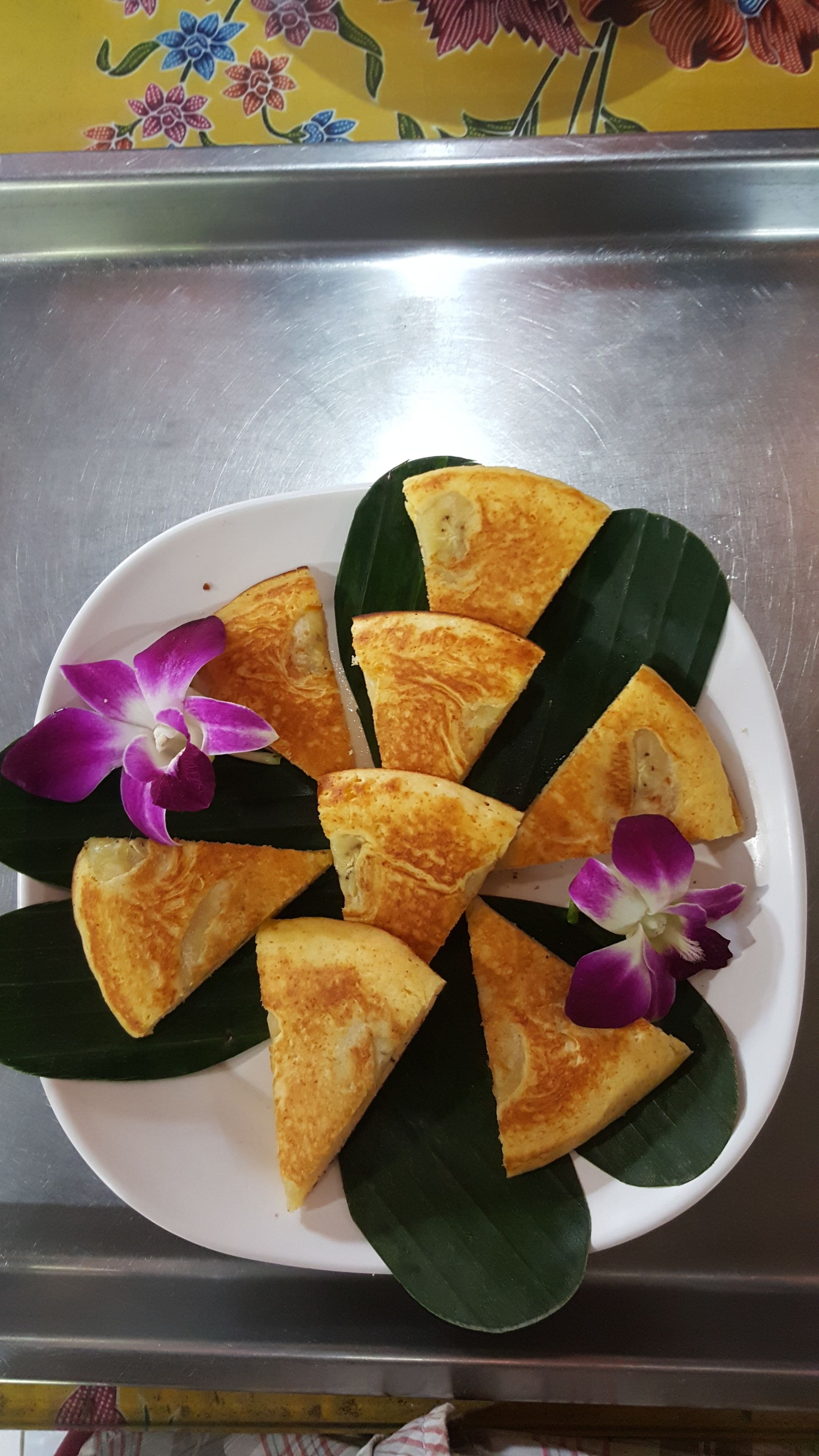 A plate of triangular food items, possibly a type of pastry, arranged on a white plate with green leaves.