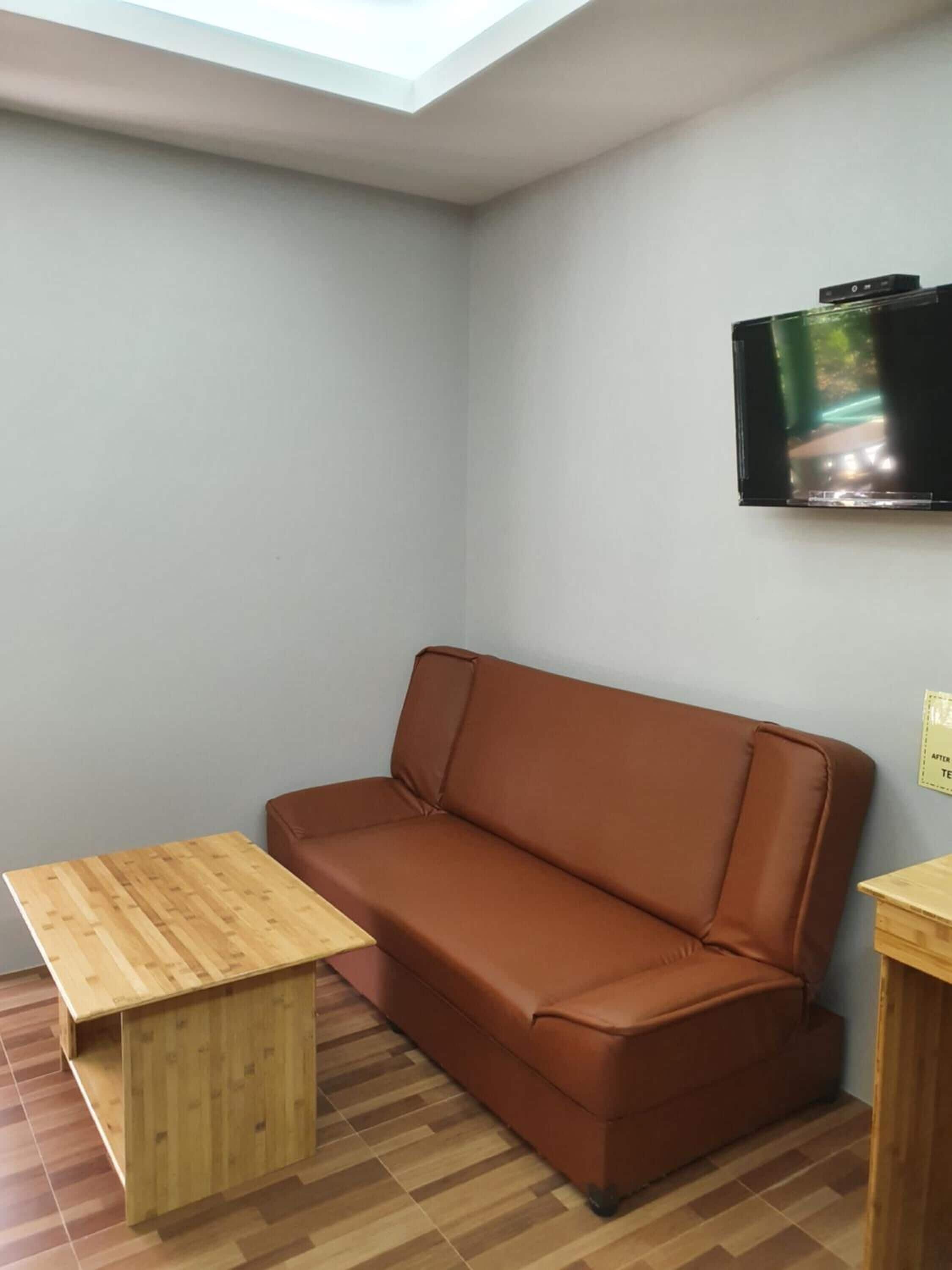 Una habitación con un sofá de cuero marrón, una mesa de madera y un televisor en la pared.