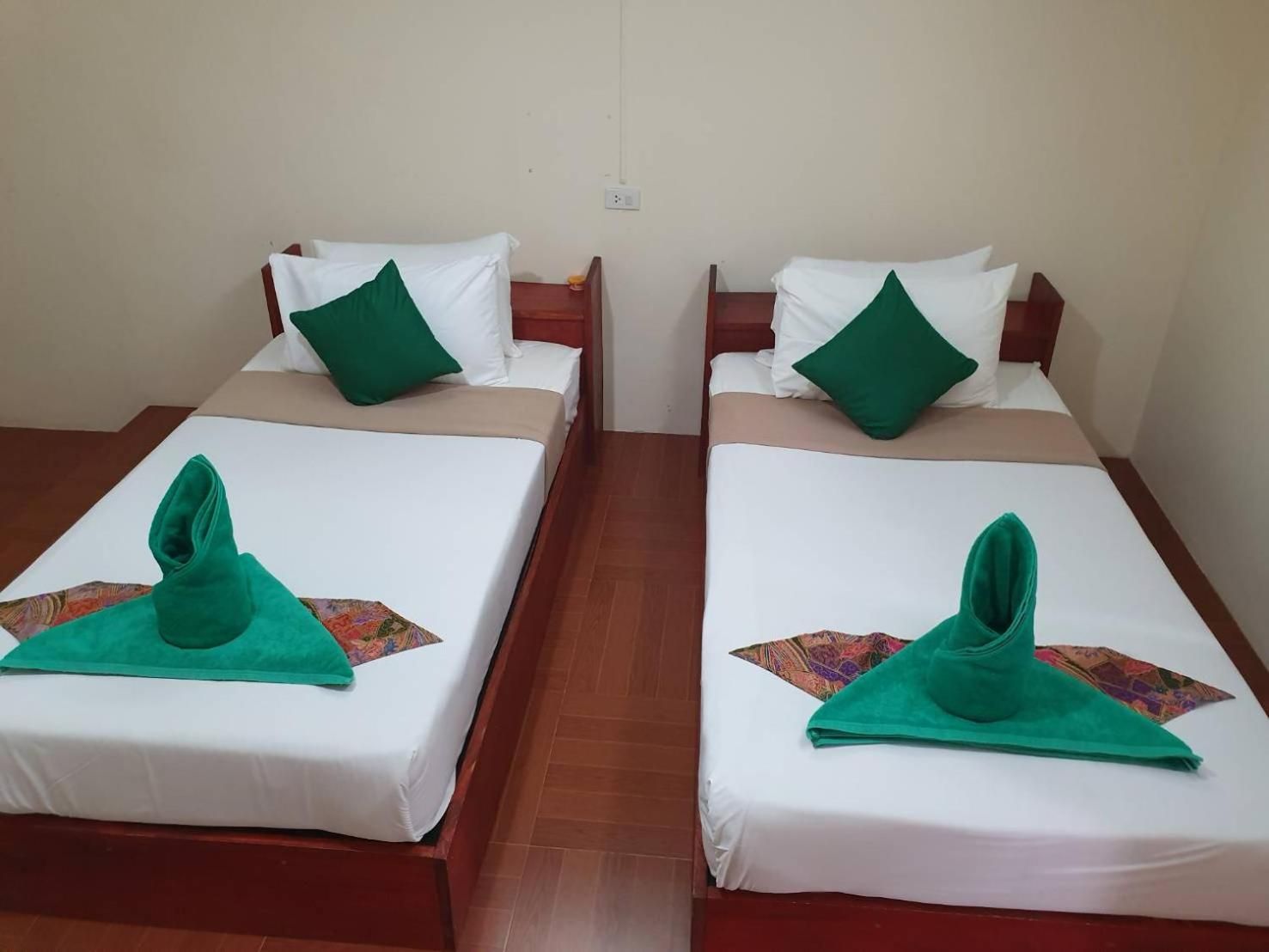 Dos camas individuales con sábanas blancas y almohadas verdes, cada una con una toalla verde doblada sobre la cama.