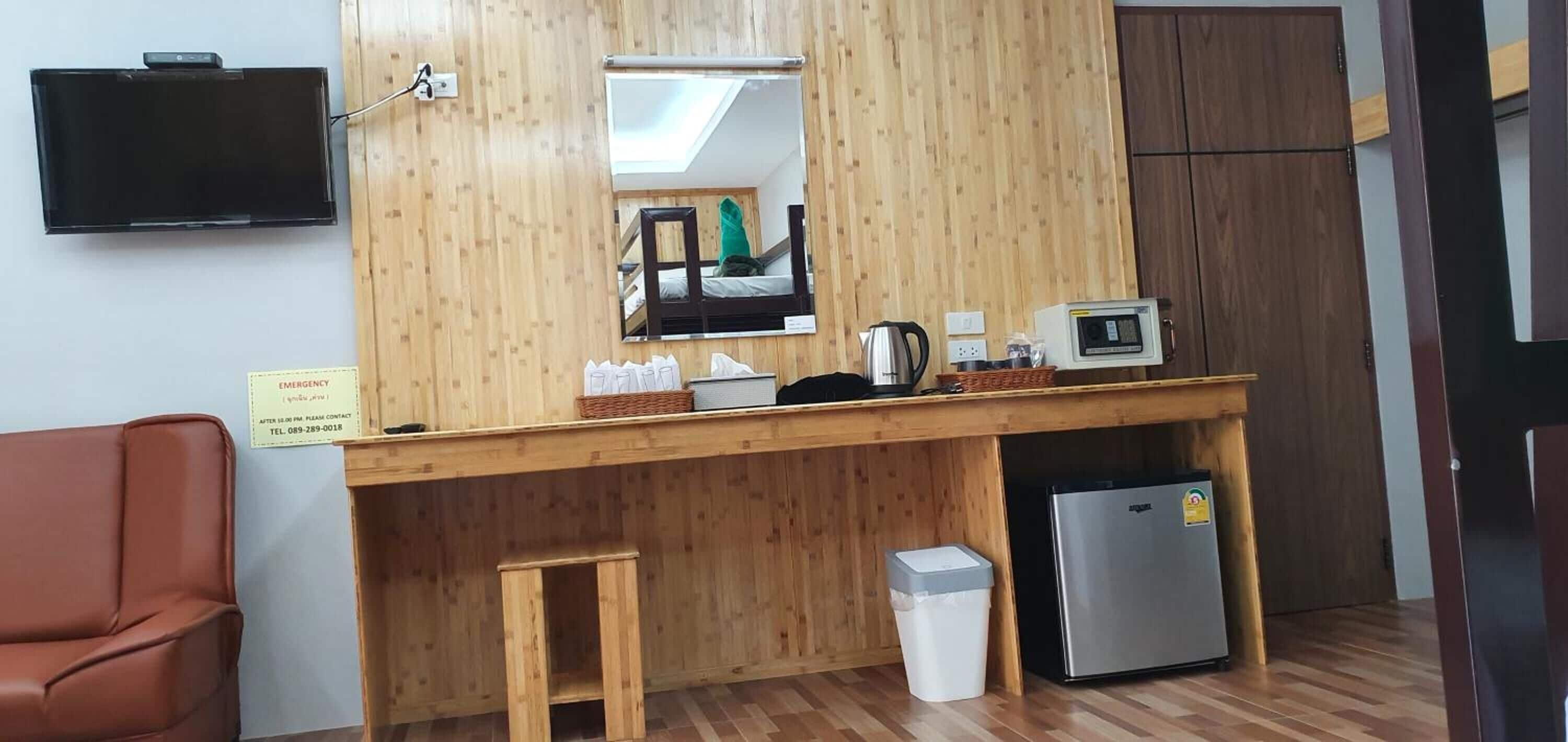 A wooden counter with a mirror, a television, a refrigerator, and a trash bin.