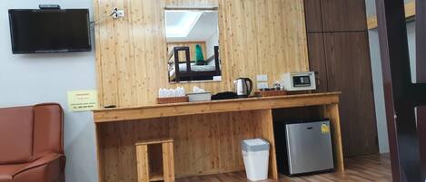 A wooden counter with a mirror, a television, a refrigerator, and a trash bin.