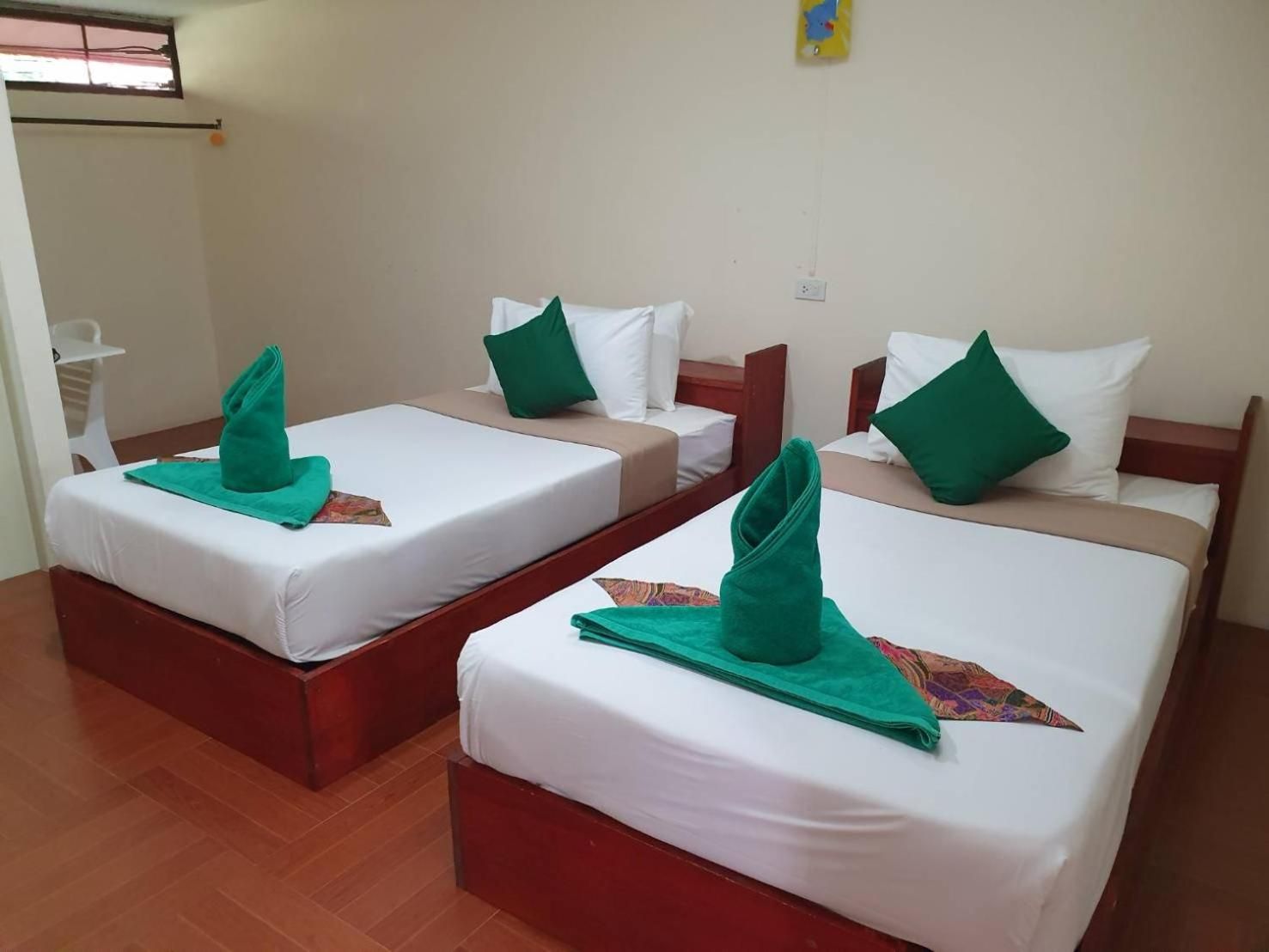 Habitación de hotel con dos camas individuales, cada una con una toalla verde y ropa de cama blanca.