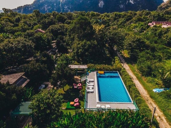 Vista aérea de una propiedad con piscina, sillones de descanso y jardín.