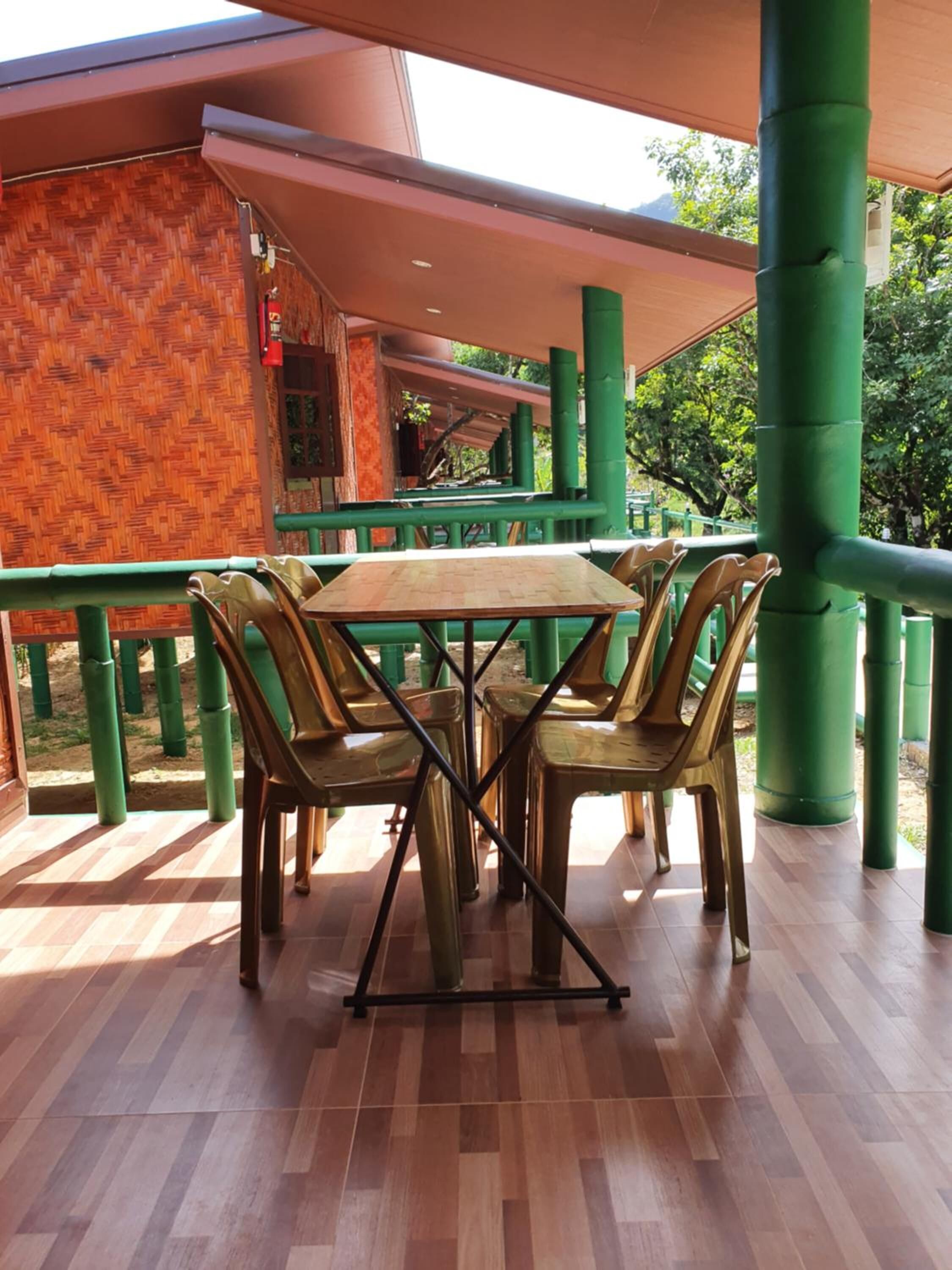 Een terras met een houten tafel en stoelen, omringd door groene hekken en zuilen.