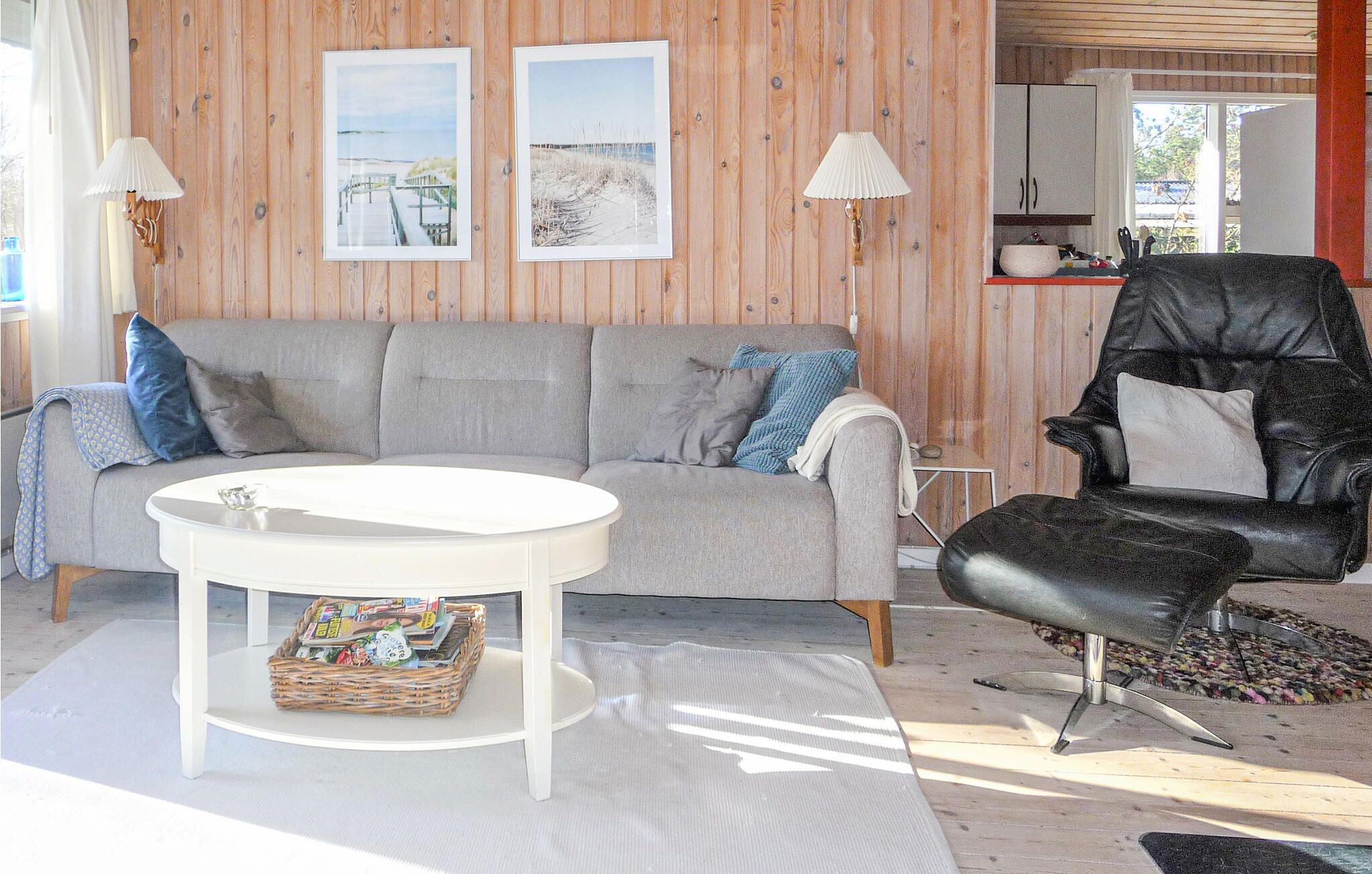 A living room with a grey sofa, a white coffee table, a black leather chair, and two framed pictures on the wall.