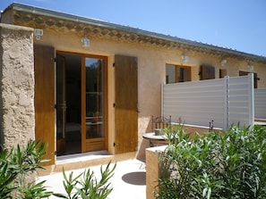 A building with a stone facade, wooden doors, and a covered patio area with plants. - Chambres d'hôtes Villa Alizé (Grimaud)
