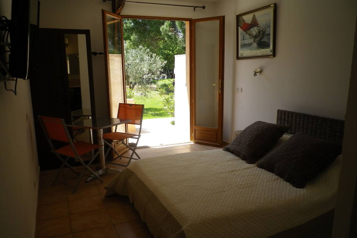 A bedroom with a bed, a chair, a small table, and a door leading to a balcony.