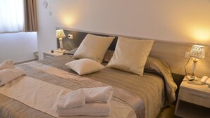 A neatly made bed with pillows and folded towels, bedside lamps, and a bedside table with a phone and a lamp. - Residenza Al Castello (Carloforte)