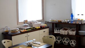 A dining area with a table set for two, a buffet counter with various food items, and a window providing natural light. - Residenza Al Castello (Carloforte)