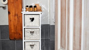 A bathroom with a white storage unit holding heart-shaped wicker baskets, a wooden door, and a tiled wall. - Residenza Al Castello (Carloforte)