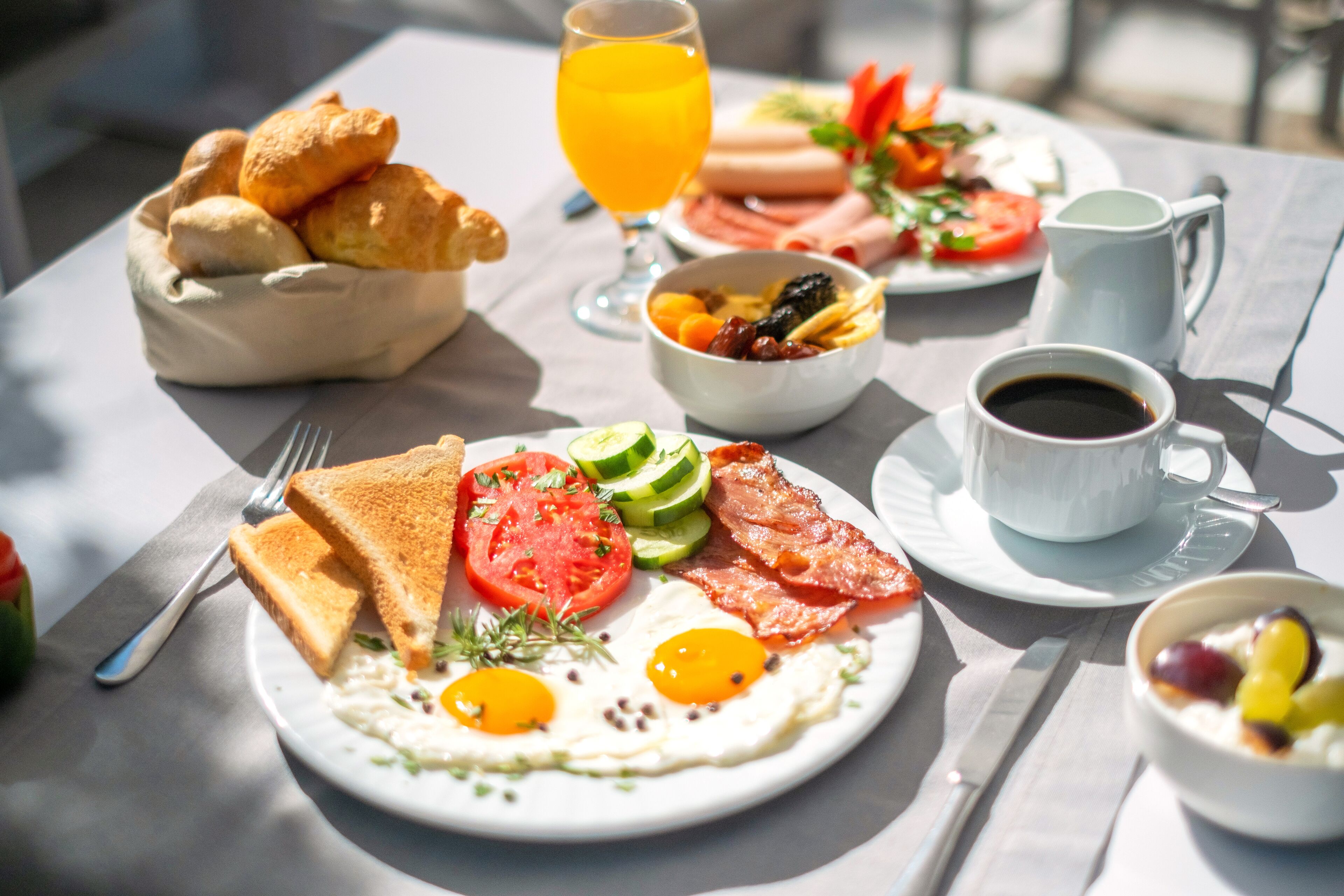 A breakfast table with toast, eggs, tomatoes, cucumbers, and a variety of fruits and vegetables.